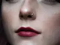 Delikatny kolczyk w nosie, jak rhino piercing, podkreśla pełne, ciemnoczerwone usta.