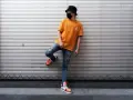 Chłopak w pomarańczowej koszulce, zniszczonych jeansach i modnych sneakersach, oparty o roletę. Stylizacja w klimacie y2k co to?