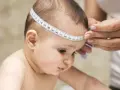 Jak zmierzyć obwód głowy dziecka? Miarka krawiecka owinięta wokół główki niemowlaka.