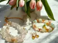 Delikatna biżuteria z kamieni, w tym naszyjnik z przezroczystych kryształów i bransoletka z pastelowych koralików, przywodzi na myśl ciepło kamienia słonecznego.