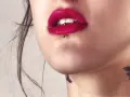 Usta z czerwoną szminką i ashley piercing. Delikatny tatuaż na szyi dodaje uroku.