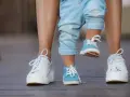 Małe niebieskie buciki dziecka obok białych butów dorosłego. Rozmiar buta dziecka a wiek, rosną stópki.