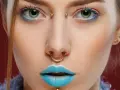 Kobieta z błękitnymi ustami i złotym septum. Jej oczy podkreślone są niebieskim cieniem, a między brwiami widoczny jest bridge piercing.