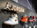 Na wystawie butów Jordan, białe Air Jordan 1 z złotymi akcentami. Obok pomarańczowe Air Jordan 5. Czy 8 5 jaki to rozmiar buta?