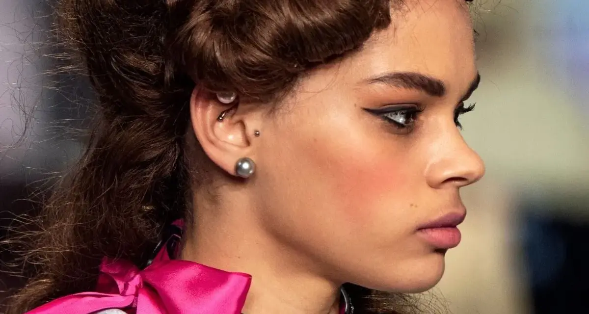 Modelka z fryzurą w stylu retro i makijażem podkreślającym oczy. W uchu widoczny jest kolczyk anti tragus.