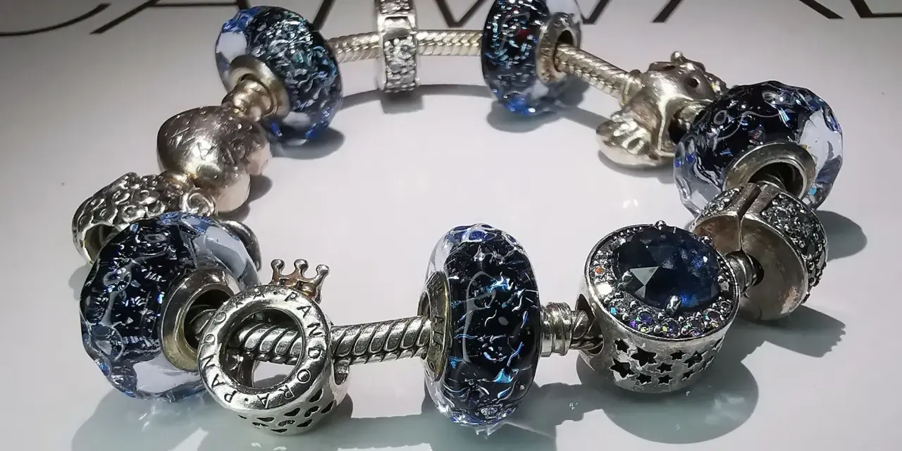 Bransoletka Pandora z niebieskimi szklanymi i srebrnymi charmsami. Zastanawiasz się, ile kosztuje naprawa bransoletki Pandora?