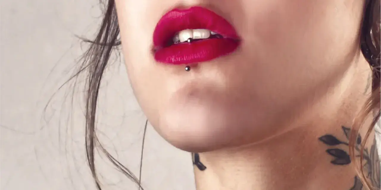 Usta z czerwoną szminką i ashley piercing. Delikatny tatuaż na szyi dodaje uroku.