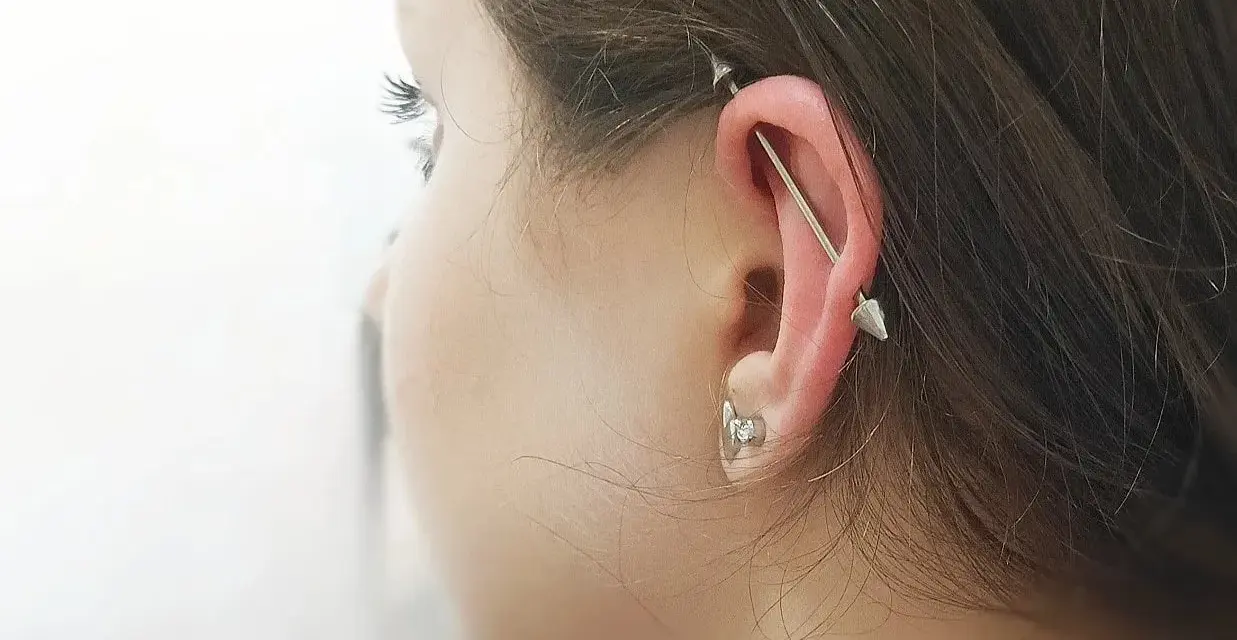Industrialny piercing ucha z długą sztangą i dwoma stożkami. To przykład, co to jest piercing, który ozdabia ciało.