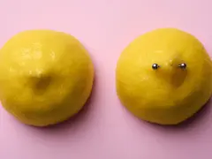 Dwa cytryny na różowym tle. Jedna cytryna ma kolczyk w sutku.