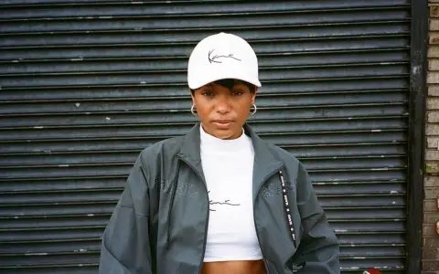 Kobieta w białej czapce z logo Karl Kani i kurtce tej marki. To kultowa marka streetwearowa.