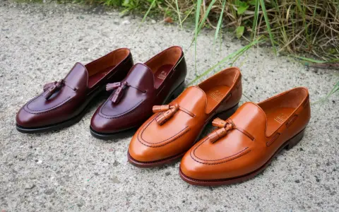 Eleganckie, skórzane loufersy z chwostami w kolorze koniaku i burgundu, ułożone na betonowej nawierzchni.