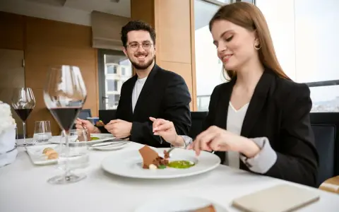 Elegancki strój na kolację do restauracji. Para w czarnych marynarkach delektuje się wykwintnym deserem przy kieliszkach czerwonego wina.