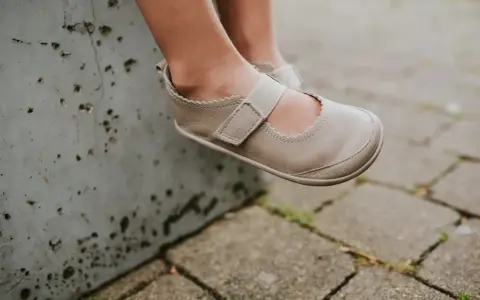 Małe stópki w beżowych balerinach z gumką, siedzące na betonowym murku.