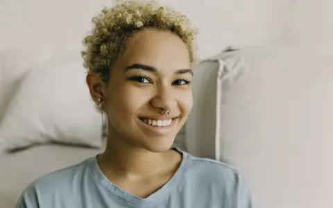 Uśmiechnięta młoda kobieta z blond kręconymi włosami i kolczykiem w nosie. Czy nostril boli? Wygląda na to, że nie!