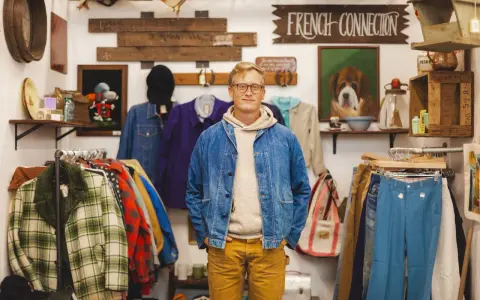 Mężczyzna w sklepie z odzieżą vintage, gdzie wisi szyld "FRENCH CONNECTION". W tle wiszą ubrania i dekoracje.
