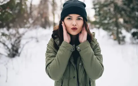 Zastanawiasz się, jaki szalik do zielonej kurtki? Ta dziewczyna w zimowym lesie ma czarną czapkę i zieloną kurtkę.