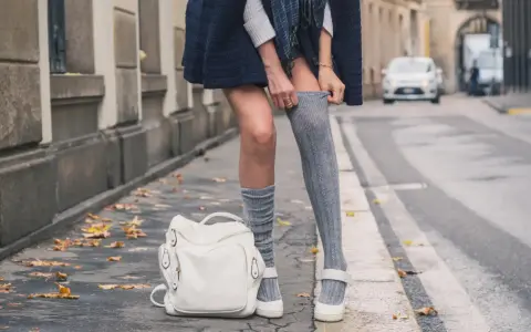 Stylizacja z długimi skarpetkami damskimi, biały plecak i jesienne liście na chodniku.