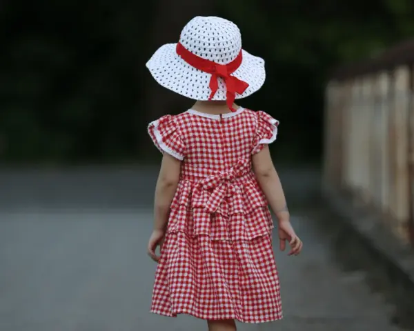 Dziewczynka w sukience w kratkę i kapeluszu z czerwoną wstążką, styl inspirowany modą lat 60.