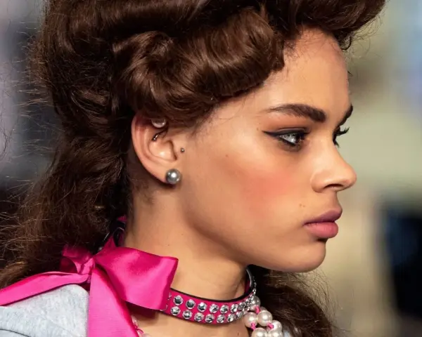 Modelka z fryzurą w stylu retro i makijażem podkreślającym oczy. W uchu widoczny jest kolczyk anti tragus.
