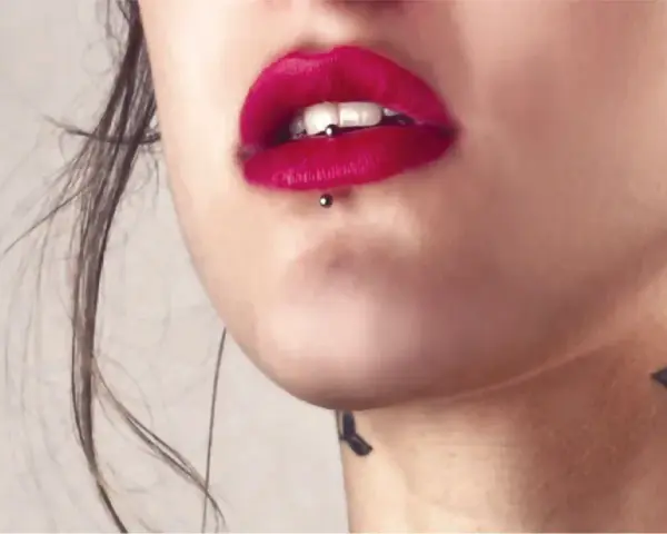 Usta z czerwoną szminką i ashley piercing. Delikatny tatuaż na szyi dodaje uroku.