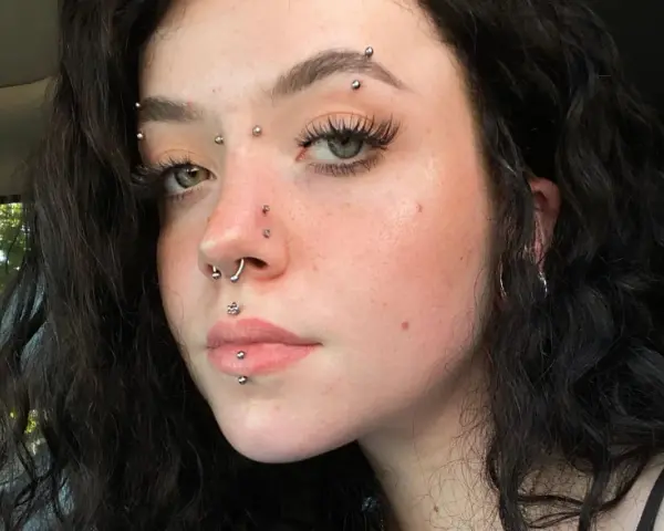 Dziewczyna z licznymi kolczykami: w nosie, ustach, brodzie i na czole. Wyróżnia się anti eyebrow piercing.