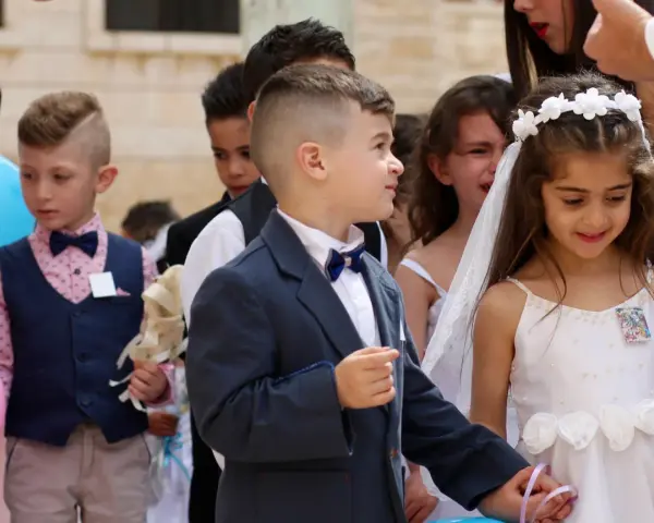Chłopiec w eleganckim garniturze, z kokardką, wygląda jak z obrazka pin-up. Obok niego dziewczynka w białej sukience.