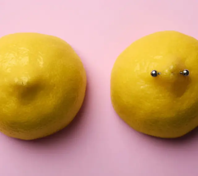 Dwa cytryny na różowym tle. Jedna cytryna ma kolczyk w sutku.