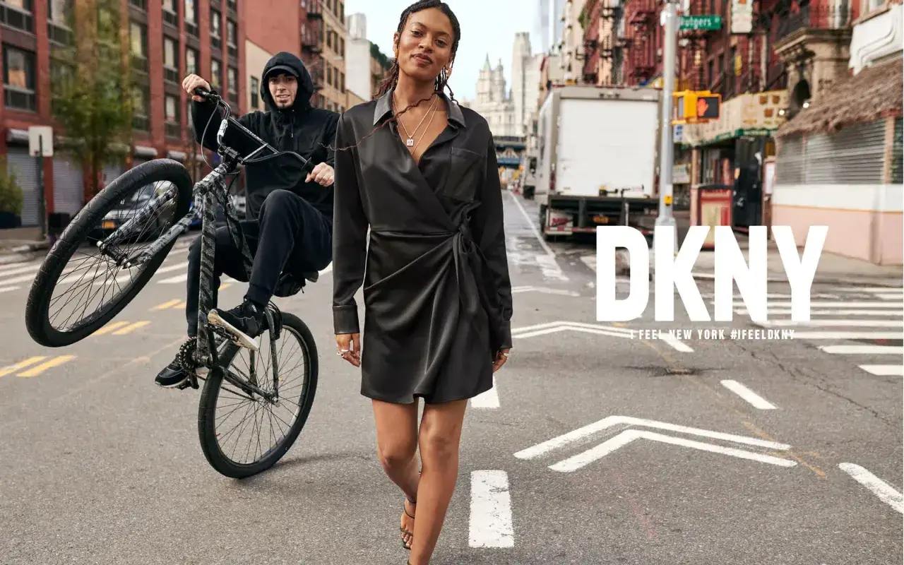 DKNY to marka, która uchwyciła ducha Nowego Jorku. Kobieta w czarnej sukience idzie ulicą, podczas gdy mężczyzna na rowerze wykonuje sztuczkę.