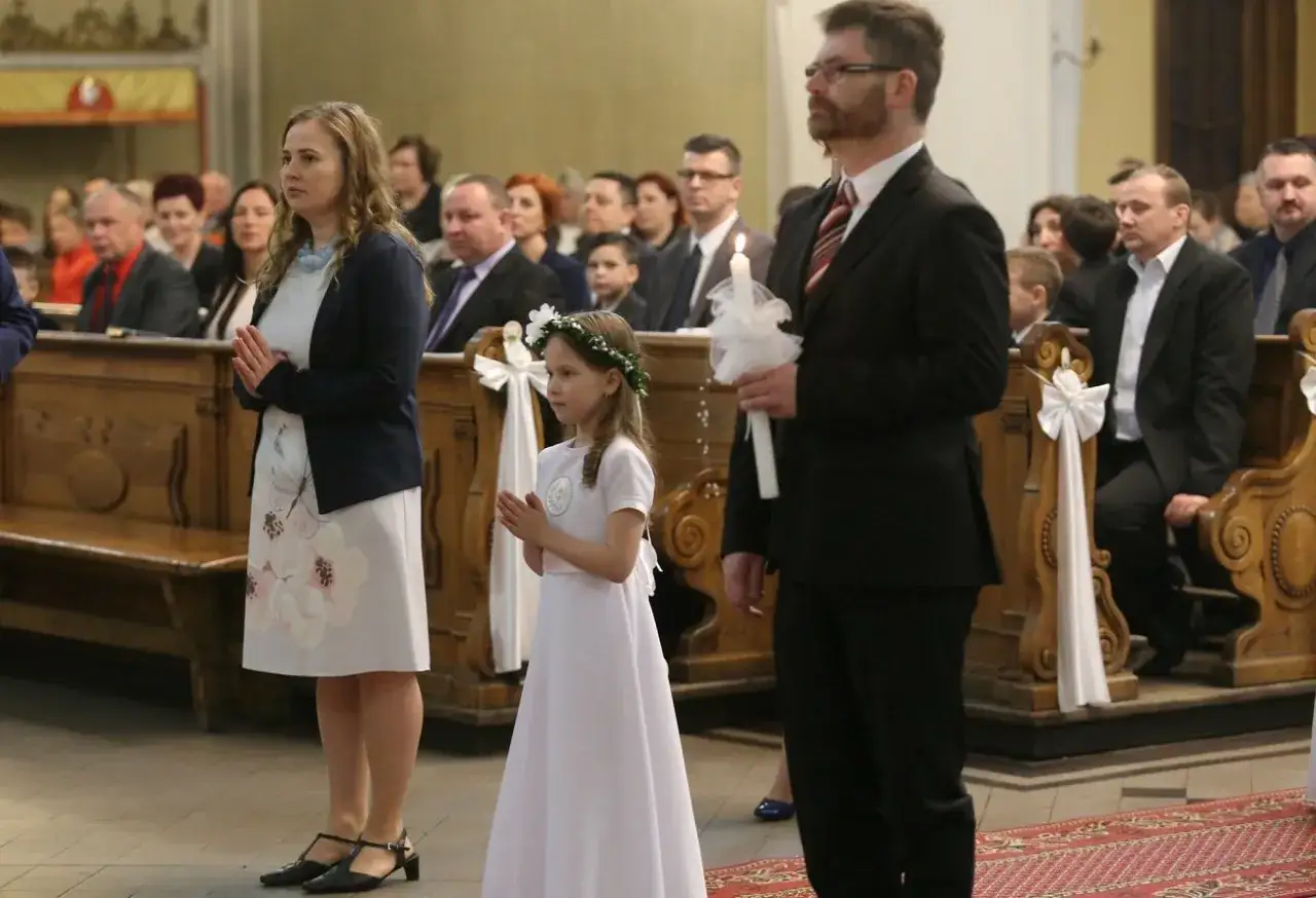 Elegancko ubrana kobieta i dziewczynka w białej sukience z wiankiem na głowie, uczestniczą w uroczystości. To inspiracja, jak się ubrać na bierzmowanie.