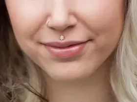 Delikatny labret co to? To ozdoba wargi w kształcie kwiatka z cyrkoniami. Obok kolczyk w nosie.
