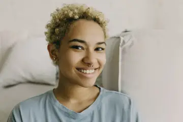 Uśmiechnięta młoda kobieta z blond kręconymi włosami i kolczykiem w nosie. Czy nostril boli? Wygląda na to, że nie!