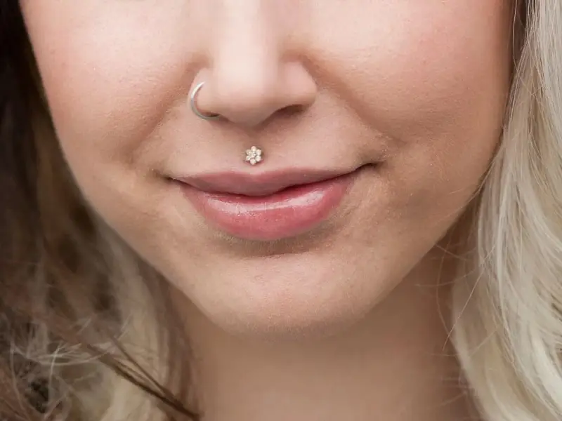 Delikatny labret co to? To ozdoba wargi w kształcie kwiatka z cyrkoniami. Obok kolczyk w nosie.