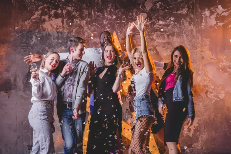 Grupa młodych ludzi świętuje, sypią się konfetti. Inspiracja, jak się ubrać do klubu: sukienka, jeansy, topy, marynarka.