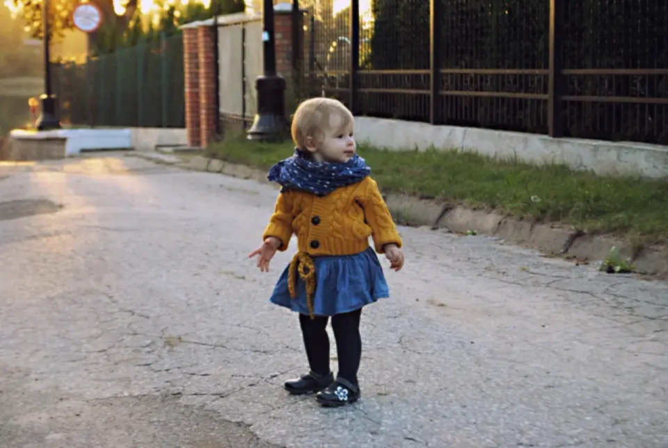 Mała dziewczynka w żółtym sweterku i niebieskiej spódniczce, z chustką na szyi, wygląda jak mały tomboy.